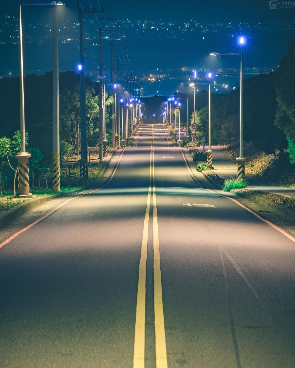 台中大肚藍色公路夜景,筆直道路在路燈照映下延伸至遠方,可眺望城市燈火與山城景致。